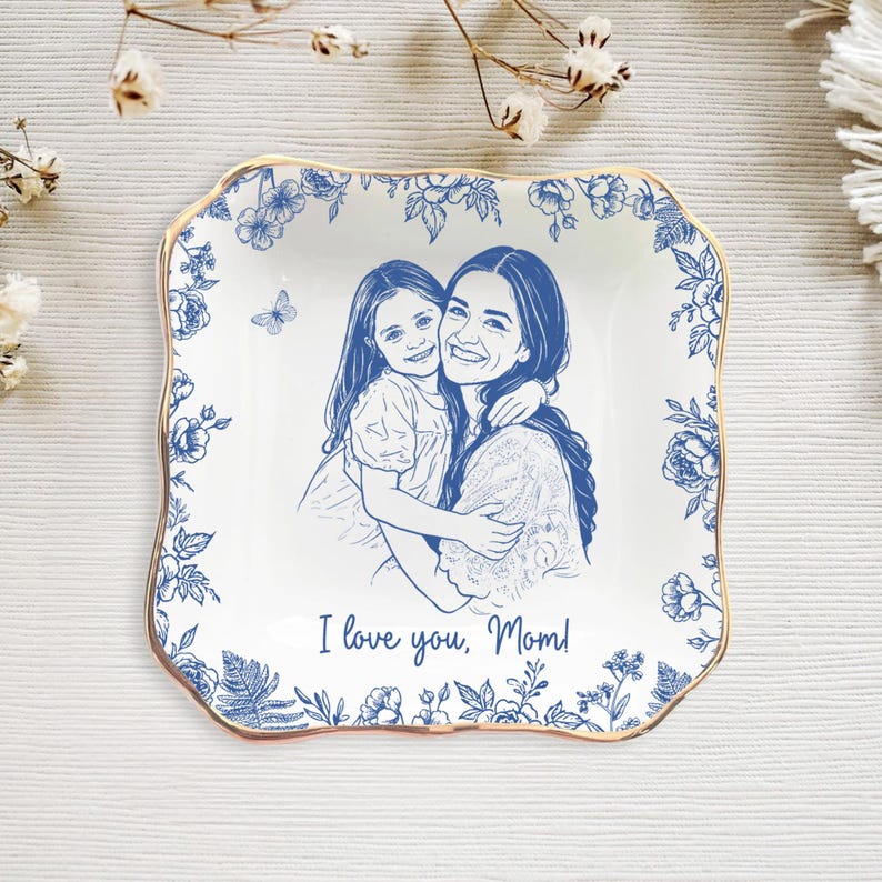 Puede incluir: Plato cuadrado de cer&aacute;mica blanca con borde floral azul y ribete dorado. El centro presenta un dibujo lineal azul de una madre y un ni&ntilde;o abraz&aacute;ndose, con el texto "I love you, Mom!"
