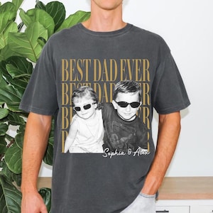 Pode incluir: Camiseta cinza escuro com o texto "BEST DAD EVER" em letras douradas. A camiseta apresenta uma foto em preto e branco de duas crian&ccedil;as usando &oacute;culos de sol. Os nomes "Sophia & Alex" s&atilde;o impressos abaixo.