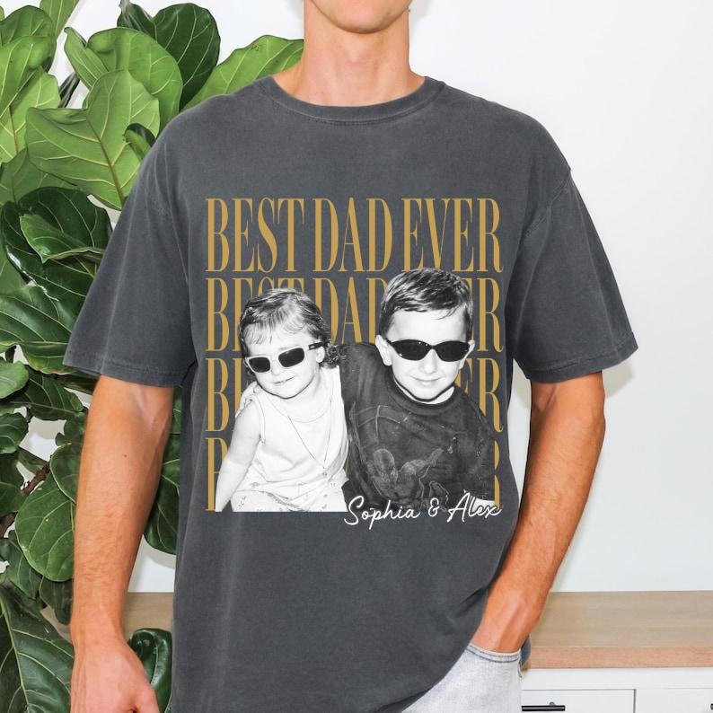 Pode incluir: Camiseta cinza escuro com o texto "BEST DAD EVER" em letras douradas. A camiseta apresenta uma foto em preto e branco de duas crian&ccedil;as usando &oacute;culos de sol. Os nomes "Sophia & Alex" s&atilde;o impressos abaixo.