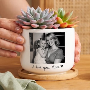 May include: White ceramic planter with a black and white photo of a mother and child. The planter holds a succulent plant with green, pink, and orange leaves. The text "I love you, Mom" is written on the planter.