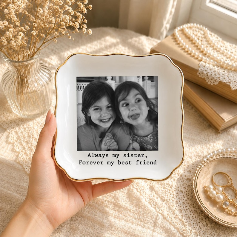 K&ouml;nnte beinhalten: Eine wei&szlig;e Keramik-Schmuckschale mit goldenem Rand, die ein Schwarz-Wei&szlig;-Foto von zwei l&auml;chelnden M&auml;dchen zeigt. Auf der Schale steht der Text "Always my sister, Forever my best friend".