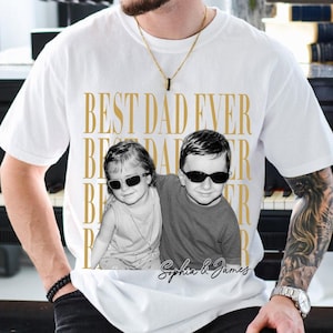 Pode incluir: Camiseta branca com a frase dourada "BEST DAD EVER". A camiseta apresenta uma foto em preto e branco de duas crian&ccedil;as usando &oacute;culos de sol. Os nomes "Sophia & James" est&atilde;o escritos abaixo.
