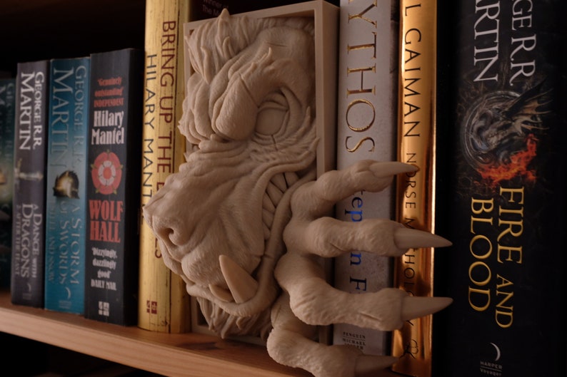 May include: A white dragon bookend with a detailed sculpted head and claws. The bookend is holding up a stack of books with titles like "Bring Up the Bodies" and "Fire and Blood".