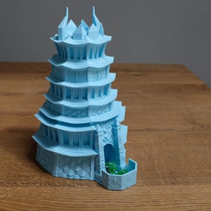 May include: A light blue 3D printed pagoda-style tower with a dice rolling tray at the base. The tower has multiple levels with windows and decorative details. Green dice are visible in the tray.