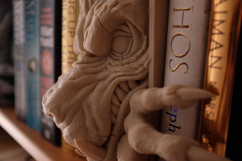 May include: A beige dragon bookend with a textured surface and a large, open mouth. The dragon is holding a book with the word "HOS" visible on the spine.