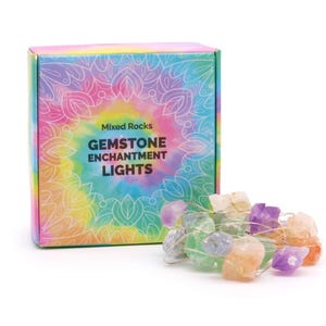 Puede incluir: Una caja de Mixed Rocks Gemstone Enchantment Lights. La caja tiene un diseño tie-dye con el nombre del producto en verde y blanco. Una cadena de piedras preciosas de colores está al lado de la caja, con piedras moradas, naranjas, verdes y transparentes.