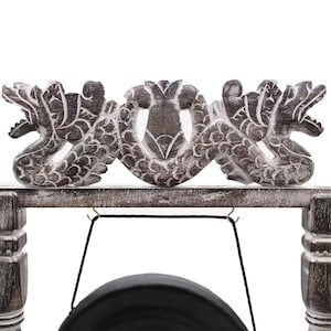 May include: A wooden gong stand with a carved dragon design. The stand is made of weathered wood and features a black gong suspended from a black cord. The dragon carvings are detailed and add a decorative element to the instrument.
