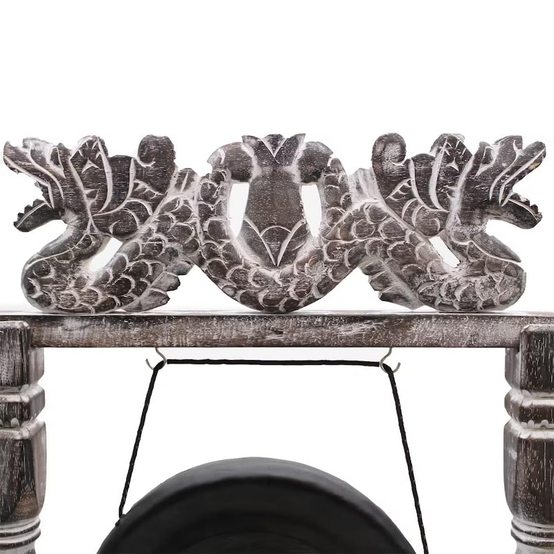 May include: A wooden gong stand with a carved dragon design. The stand is made of weathered wood and features a black gong suspended from a black cord. The dragon carvings are detailed and add a decorative element to the instrument.
