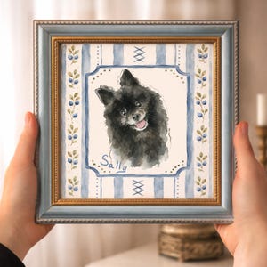 Pode incluir: Uma pintura em aquarela emoldurada de formato quadrado apresentando um cão preto fofo com o nome Sally escrito em azul abaixo. A arte está sobre um fundo de listras verticais azuis e uma borda de pequenas bagas azuis e folhas verdes.
