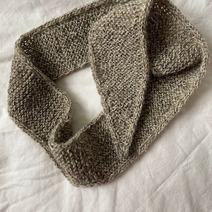 Może przedstawiać: Brązowy, dziany szalik wykonany z miękkiej, fakturowanej przędzy. Szalik jest złożony na pół i ma prosty, klasyczny wzór.