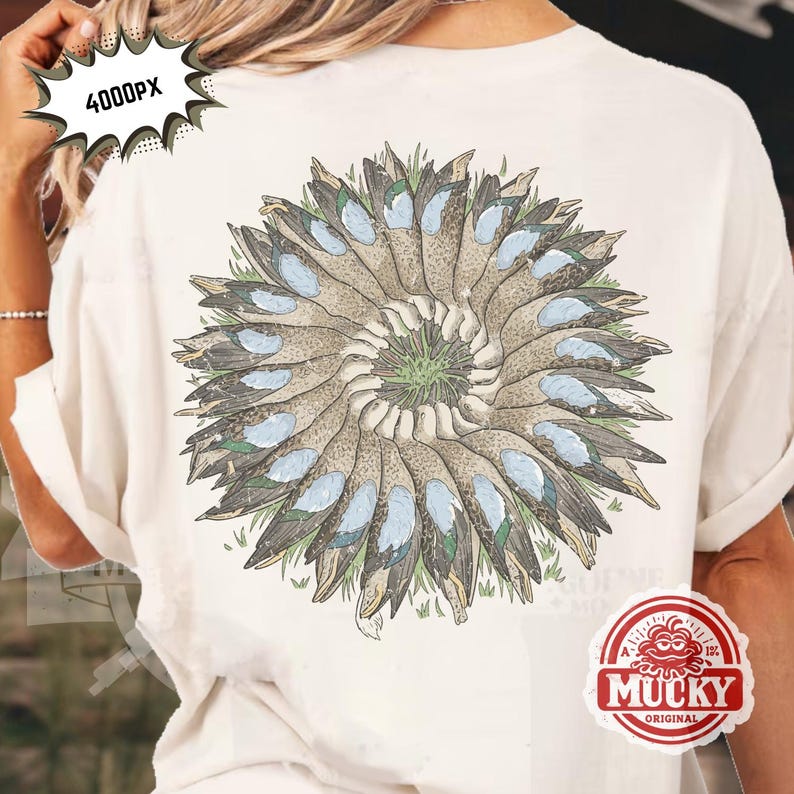 May include: Cream-coloured t-shirt with a detailed illustration of a circular arrangement of duck wings and feathers. The design incorporates shades of brown, blue, and green, creating a nature-inspired aesthetic. The shirt has a relaxed fit.