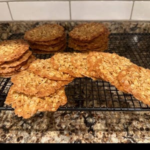 May include: A close-up of a wire rack with a large batch of freshly baked oatmeal cookies. The cookies are golden brown and have a crispy texture.