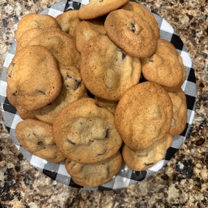 May include: A plate of freshly baked chocolate chip cookies. The cookies are golden brown and have a slightly crispy texture. They are arranged in a pile on a black and white checkered plate.