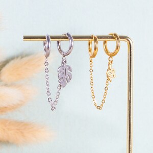May include: Two pairs of earrings with dangling chains. One pair is silver with a leaf charm and the other is gold with a leaf charm.