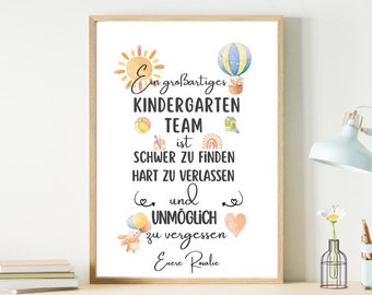 May include: A white framed print with a quote about a kindergarten team. The quote reads "Ein großartiges KINDERGARTEN TEAM ist SCHWER ZU FINDEN HART ZU VERLASSEN und UNMÖGLICH zu vergessen. Eure Rovalic". The print features colorful illustrations of a sun, a hot air balloon, a rainbow, and a heart.