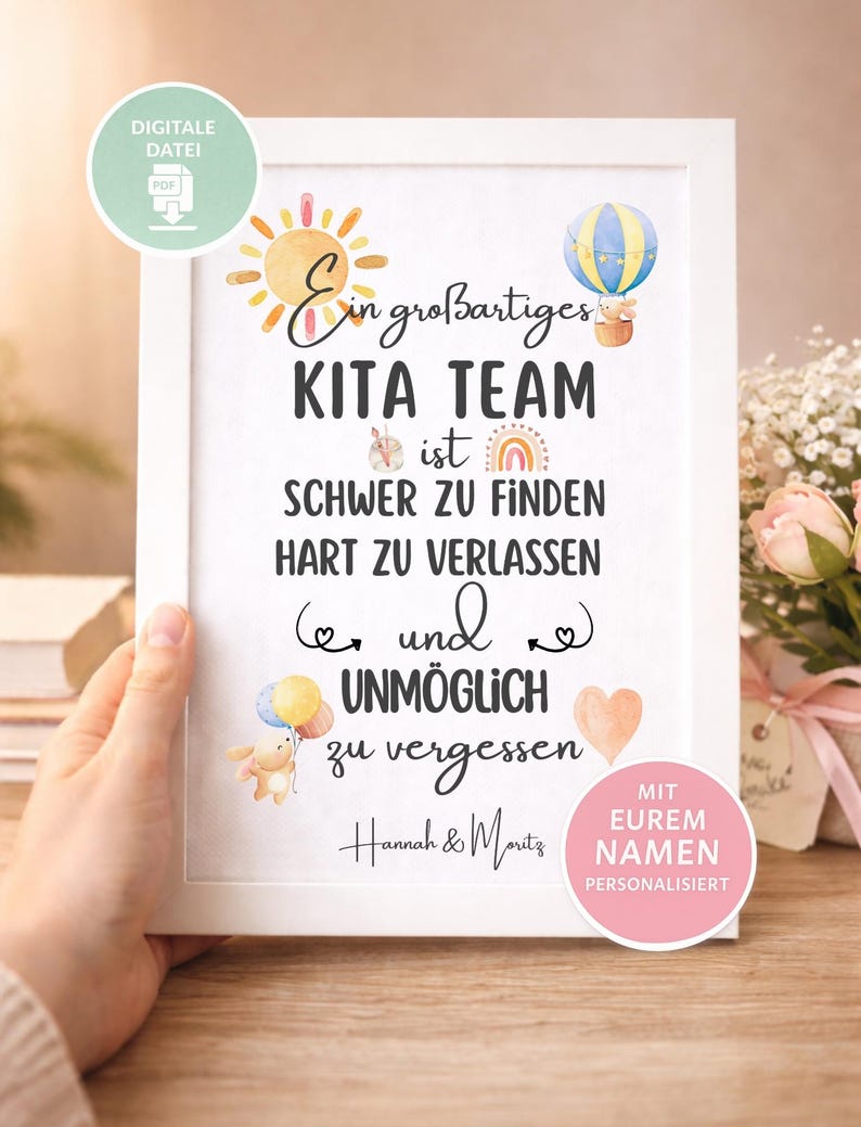 May include: A framed print with the text "Ein gro&szlig;artiges KITA TEAM ist SCHWER ZU FINDEN HART ZU VERLASSEN und UNM&Ouml;GLICH zu vergessen." The print features watercolor illustrations of a sun, hot air balloon, rainbow, and bear with balloons. The frame is white.