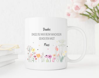 Puede incluir: Taza de cerámica blanca con un diseño floral y el texto "Danke. Dass du mir beim wachsen geholfen hast Maxi". La taza presenta un borde de flores silvestres de colores con flores rosas, amarillas y naranjas.