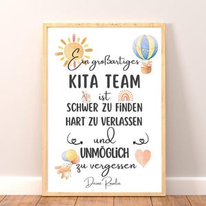 May include: A framed print with the text "Ein gro&szlig;artiges KITA TEAM ist SCHWER ZU FINDEN HART ZU VERLASSEN und UNM&Ouml;GLICH zu vergessen Deine Rosalie." The print features watercolor illustrations of a sun, hot air balloon, rainbow, and heart.