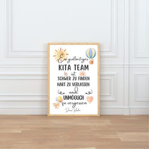 May include: A framed print with the text "Ein gro&szlig;artiges KITA TEAM ist SCHWER ZU FINDEN HART ZU VERLASSEN und UNM&Ouml;GLICH zu vergessen Deine Roalie." The print features watercolor illustrations of a sun, hot air balloon, rainbow, and hearts.