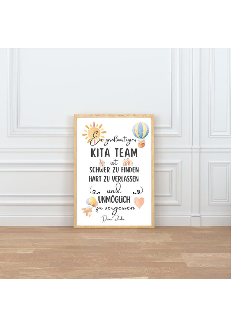May include: A framed print with the text "Ein gro&szlig;artiges KITA TEAM ist SCHWER ZU FINDEN HART ZU VERLASSEN und UNM&Ouml;GLICH zu vergessen Deine Roalie." The print features watercolor illustrations of a sun, hot air balloon, rainbow, and hearts.