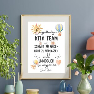 May include: Framed print with the text "Ein gro&szlig;artiges KITA TEAM ist SCHWER ZU FINDEN HART ZU VERLASSEN und UNM&Ouml;GLICH zu vergessen Deine Roralie." The print features watercolor illustrations of a sun, hot air balloon, rainbow, and teddy bear.