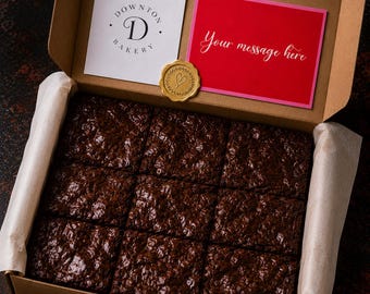 May include: A box of freshly baked brownies from Downton Bakery, with a red card that says "Your message here". The box also includes a gold seal with a heart design.