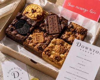 May include: A selection of baked treats in an open cardboard box. The box contains brownies, blondies, and biscuits. The box also includes a card that says "Your message here". The box is branded with the "Downton Bakery" logo and a menu of the treats.
