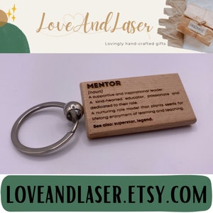 May include: Wooden keychain with a definition of the word "mentor" engraved on it. The keychain is brown and has a silver ring. The text on the keychain reads: "[noun] A supportive and inspirational leader. A kind-hearted educator, passionate and dedicated to their role. A nurturing role model that plants seeds for lifelong enjoyment of learning and teaching. See also: superstar, legend."