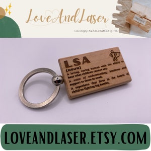 May include: Wooden keyring with a silver ring. The keyring has a definition of the word "LSA" engraved on it. The definition reads: "A loving, caring human with the ability to hear what children cannot say. A voice of understanding, kindness and support to those in need. A superhero that lives in the hearts of children fighting big battles."