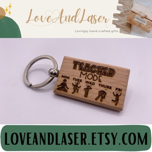 May include: Wooden keychain with the text "Teacher Mode" and a series of stick figures representing different days of the week. The keychain is attached to a silver key ring.