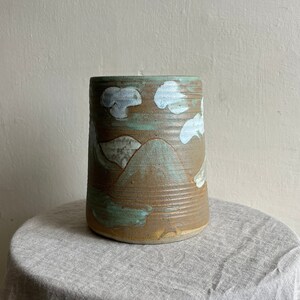 May include: A ceramic vase with a brown, green and white glaze. The vase features a mountain and cloud design.
