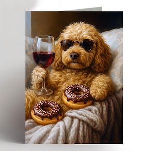 May include: A greeting card showing a golden doodle wearing sunglasses, holding a glass of red wine, and two chocolate-frosted donuts. The dog is seated on a white knitted blanket.