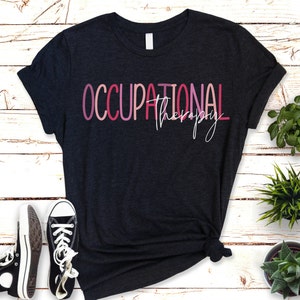 May include: A dark gray t-shirt with the text "OCCUPATIONAL therapy" in pink, red, and white lettering.