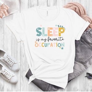 May include: White t-shirt with the text "SLEEP is my favorite OCCUPATION" in colorful letters with stars. The text is in a playful font.