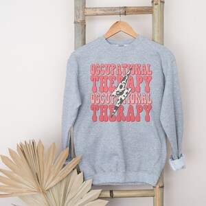 May include: Gray sweatshirt with a pink and white lightning bolt graphic and the text "Occupational Therapy" repeated twice.