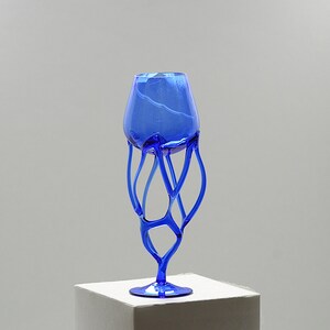 Peut inclure: Un gobelet en verre bleu avec un pied unique, abstrait et complexe. Le pied est fait de verre torsadé et incurvé, créant un aspect fluide et organique.