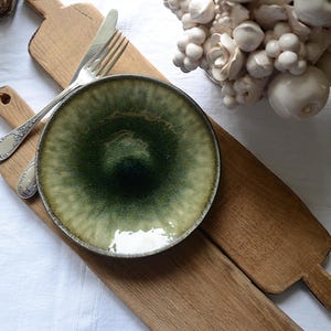 Peut inclure: Une assiette en céramique verte et blanche avec un glaçage texturé. L'assiette est sur une planche à découper en bois avec une poignée.