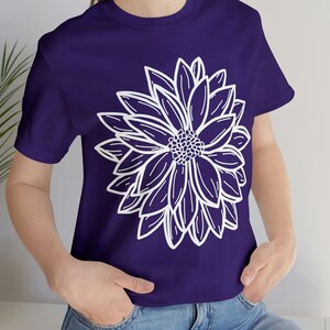 Könnte beinhalten: Ein lila T-Shirt mit einer weißen Umrandung einer großen Blume.