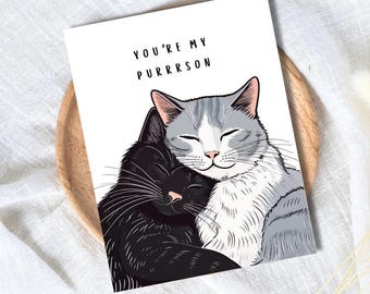 Może przedstawiać: Kartka z pozdrowieniami przedstawiająca czarnego kota i szaro-białego kota obejmujących się. U góry wydrukowano napis "YOU'RE MY PURRRSON". Koty mają zamknięte oczy i różowe nosy, wyrażając uczucie.