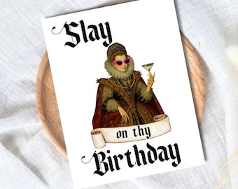 May include: A white greeting card with the words "Slay on thy Birthday" in black gothic font. The card features a vintage illustration of a woman wearing pink sunglasses and holding a cocktail. The card is on a wooden plate.