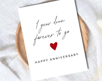 May include: A white anniversary card with the text "1 year down forever to go" in black script. A small red heart is below the text, and "HAPPY ANNIVERSARY" is printed at the bottom.