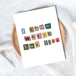 May include: A white rectangular card featuring the text "i know where you live" displayed in a ransom note style. Each letter is printed on a small, individual rectangular paper cutout in various colors including blue, tan, pink, yellow, and green.