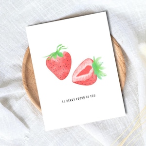 Könnte beinhalten: Weiße Grußkarte mit Aquarellillustrationen von zwei Erdbeeren. Eine Erdbeere ist ganz, die andere halbiert. Der Text "So berry proud of you" ist unter den Illustrationen aufgedruckt.