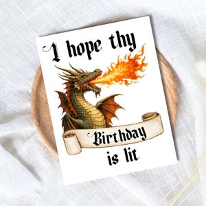 Puede incluir: Tarjeta de felicitación con una ilustración de un dragón que escupe fuego. La tarjeta dice "I hope thy Birthday is lit" en una fuente gótica. El dragón es marrón, dorado y naranja.