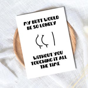 May include: A white greeting card with black text that reads MY BUTT WOULD BE SO LONELY WITHOUT YOU TOUCHING IT ALL THE TIME, featuring a simple black line drawing of buttocks in the centre of the card between the two lines of text.
