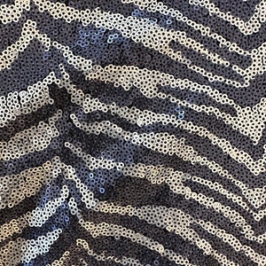 May include: Close-up of a fabric with a sequined zebra stripe pattern. The sequins are in shades of silver and navy blue, creating a shimmering effect. The design features a repeating chevron pattern.