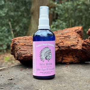 Könnte beinhalten: Eine blaue Sprühflasche mit weißem Pumpkopf und rosa Etikett. Das Etikett enthält den Text Urukla's Magic Remedies, Native Wisdom, smudge spray, White Sage & Lavender sowie 3.5 FL OZ (100ml) und eine Grafik einer Person mit Kopfschmuck.