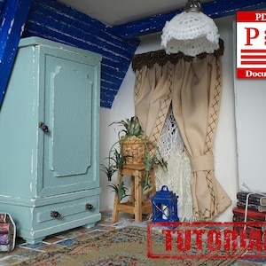 Puede incluir: Una habitación de casa de muñecas en miniatura con un armario azul claro, una pequeña planta en una cesta de mimbre, una cortina marrón con un ribete de encaje blanco y una linterna azul. La habitación tiene un suelo de madera y una alfombra con un patrón floral. El texto "TUTORIAL" es visible en rojo.