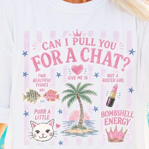 May include: A white t-shirt featuring a pink striped background and the text "CAN I PULL YOU FOR A CHAT?" along with illustrations of two fish, a heart, a palm tree, a lipstick, a cat face, and a crown, accompanied by phrases like "GIVE ME 10".