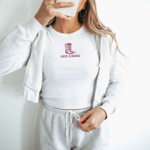 May include: White cropped t-shirt with a maroon graphic of cowboy boots and the text "SAVE A HORSE".